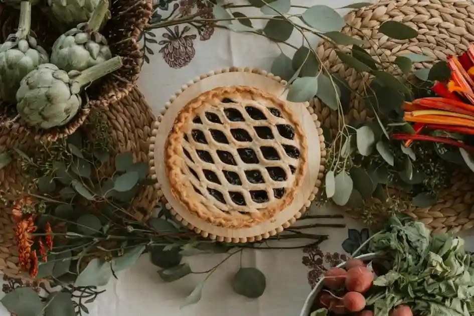 A lattice-top pie surrounded by autumn harvest vegetables and greenery